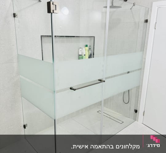 מקלחון זכוכית עם מדף ובקבוקי שמפו